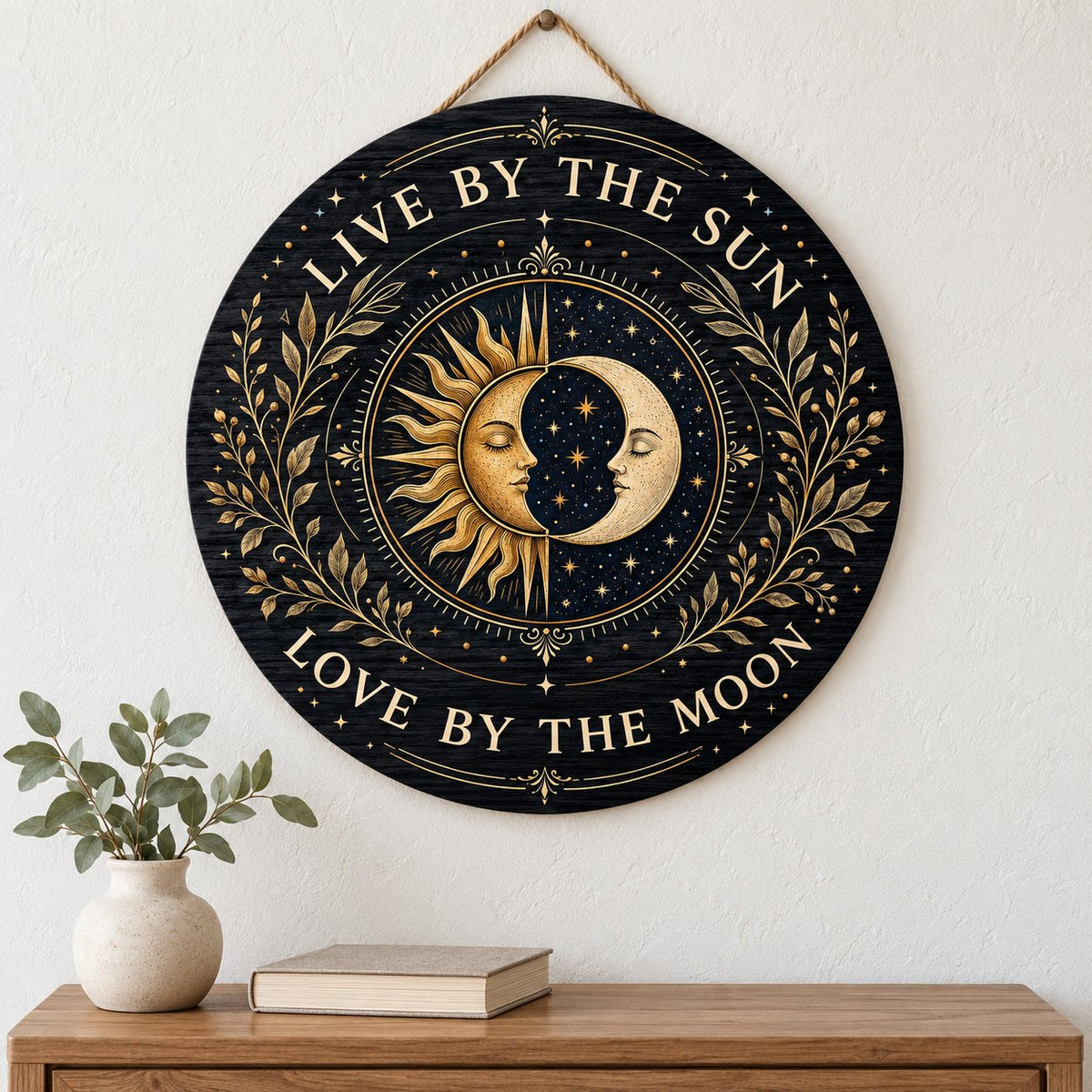 Round wooden sign with gold sun and crescent moon faces and the words “Live By The Sun, Love By The Moon”.