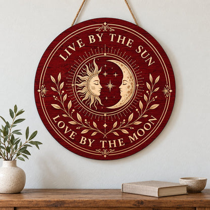 Round wooden sign with sun and crescent moon faces, stars, vines, and the quote Live by the Sun, Love by the Moon.
