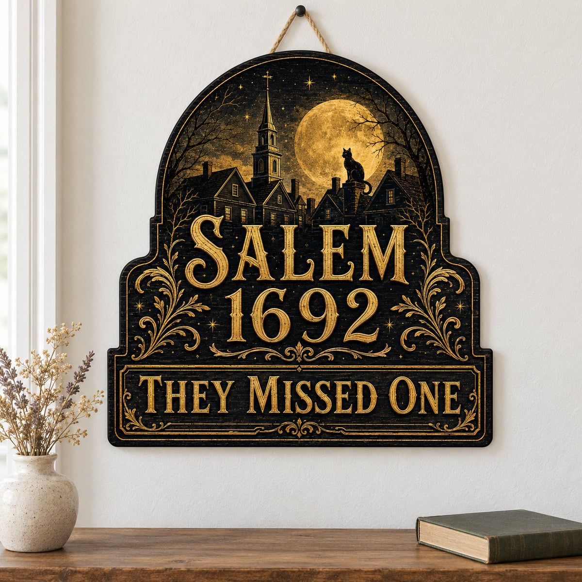 Custom-cut wooden sign reading “SALEM 1692” and “THEY MISSED ONE” with a black cat on a moonlit village and gold filigre