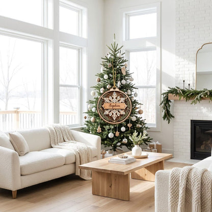 Round wood ornament with a snowflake, gemstone accents, pine sprigs, and a banner personalized with a name.