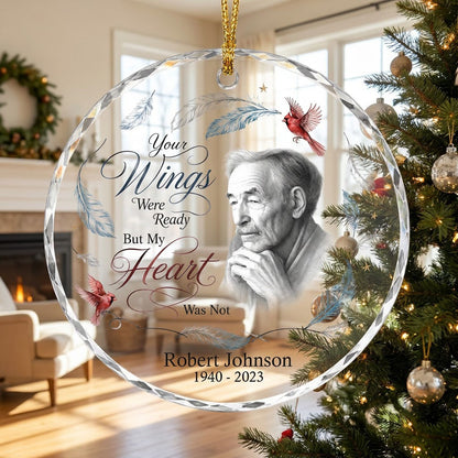 Round glass ornament with sketch portrait, two red cardinals, blue and brown feathers, and memorial name and years.