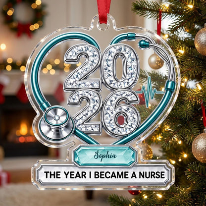 Clear acrylic ornament with a teal stethoscope heart, diamond 2026 numerals, teal ECG wave, and a personalized name bann