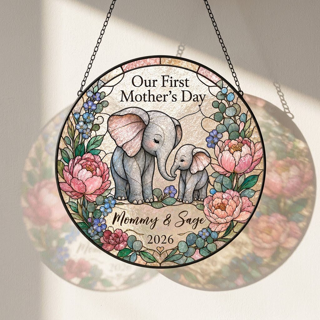 Round stained-glass suncatcher of mother and baby elephants touching trunks amid pink peonies and blue flowers.