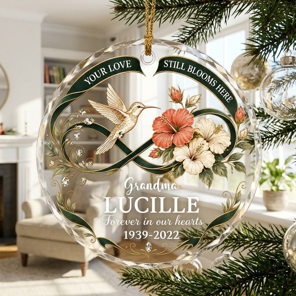 Round glass ornament with hummingbird, hibiscus, green infinity ribbon, and 'Your Love Still Blooms Here' text.