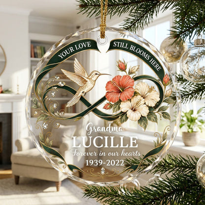 Round glass ornament with hummingbird, hibiscus, green infinity ribbon, and 'Your Love Still Blooms Here' text.