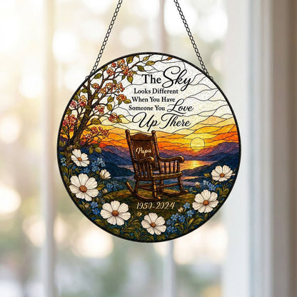Round stained glass–style suncatcher with an empty rocking chair on a hill at sunset with flowers and a lake.