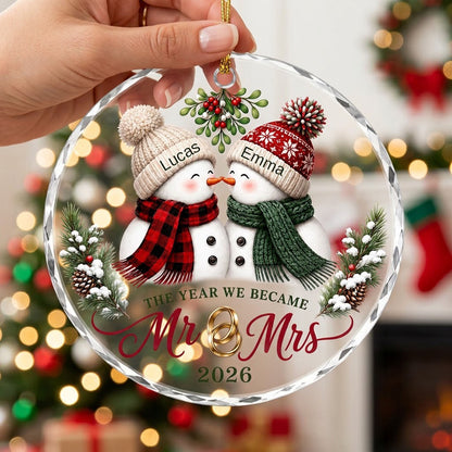 Round faceted glass ornament with two kissing snowmen under mistletoe and gold rings, personalized with names.