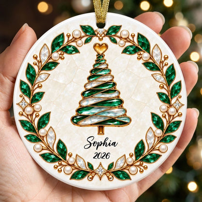 Round ceramic ornament with an emerald jeweled spiral Christmas tree and gold filigree wreath on cream.