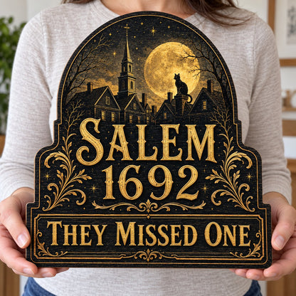 Custom-cut wooden sign reading “SALEM 1692” and “THEY MISSED ONE” with a black cat on a moonlit village and gold filigre