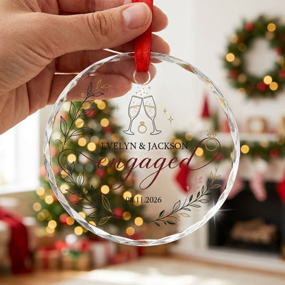 Round glass ornament with clinking champagne flutes, sparkles, ring and botanical foliage with burgundy ribbon and the w