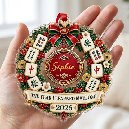 A clear acrylic wreath ornament with Mahjong tiles, red bow, gold coins, and the text THE YEAR I LEARNED MAHJONG.