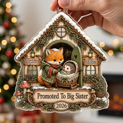 House-shaped acrylic ornament with 'Promoted To Big Sister' and a fox beside a baby hedgehog in a bassinet.