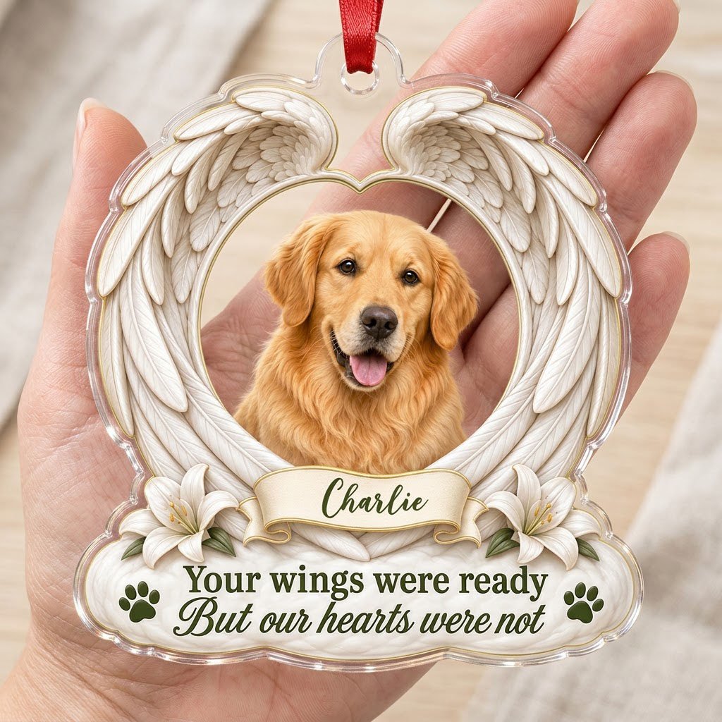 Clear acrylic angel wings ornament with a circular dog photo, white lilies, a dark green paw print, and a name banner.
