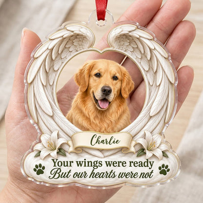 Clear acrylic angel wings ornament with a circular dog photo, white lilies, a dark green paw print, and a name banner.