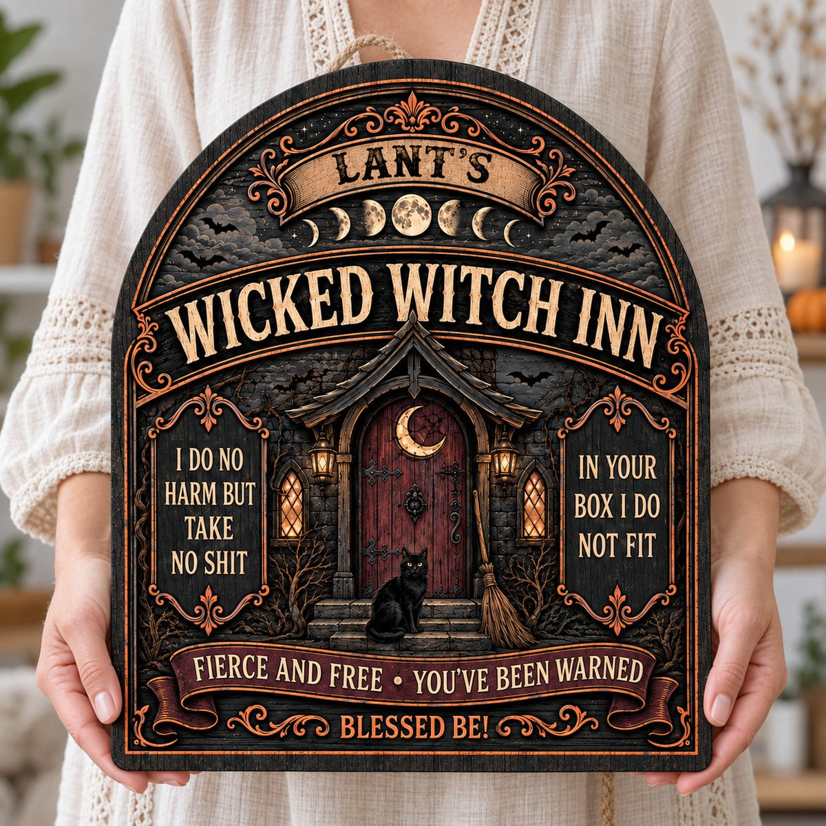Arch wooden sign with a witch's cottage, bats, moon phases, red crescent door, broom, and a black cat on the steps.