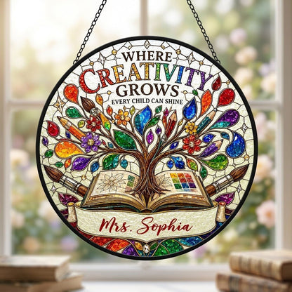 Round stained glass-style suncatcher with tree growing from an open book, paintbrushes, pencils, blossoms, and teacher n