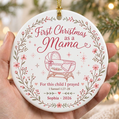 Round ceramic ornament with pink floral wreath, baby bassinet line art, stars, and First Christmas as a Mama.