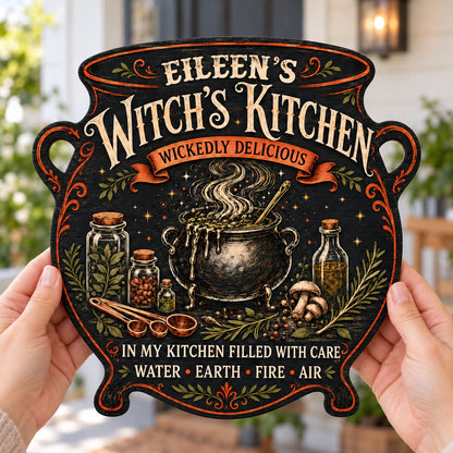 Custom-cut wooden sign shaped like a cauldron with herbs, potion jars, orange scroll and Witch's Kitchen text.