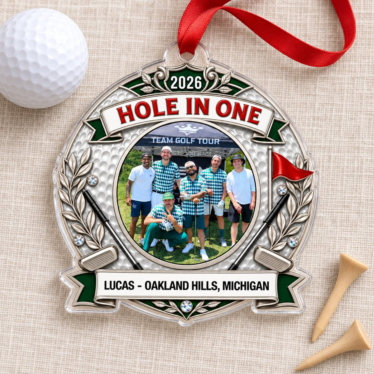Silver trophy-style golf ornament with laurel branches, crossed clubs, red flag, 2026 and HOLE IN ONE, plus a circular p