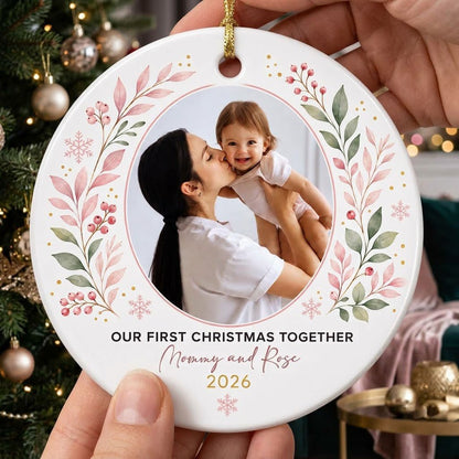 Round ceramic ornament with a photo frame, pink-green botanical wreath, and 'OUR FIRST CHRISTMAS TOGETHER' text.