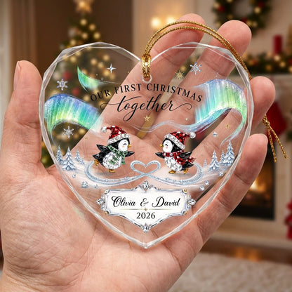Heart glass ornament with two ice-skating penguins under green and blue aurora with names and date.