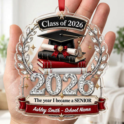 Acrylic ornament shows Class of 2026 text, cap, diploma, jeweled laurel wreath and banners personalized with name and sc