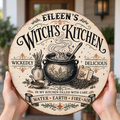 Round wooden hanging sign with a bubbling cauldron, herbs, spellbook, stars and the words Witch's Kitchen.