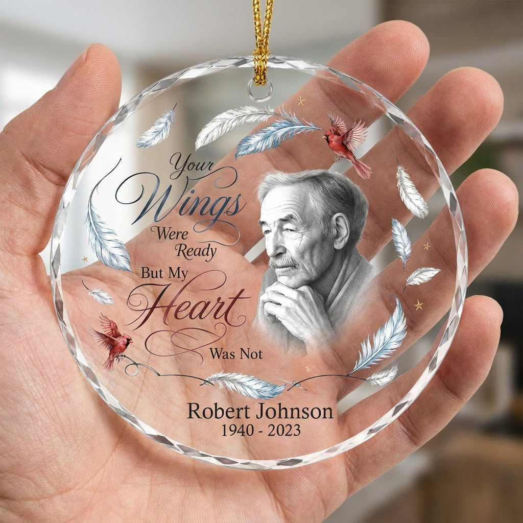 Round glass ornament with sketch portrait, two red cardinals, blue and brown feathers, and memorial name and years.