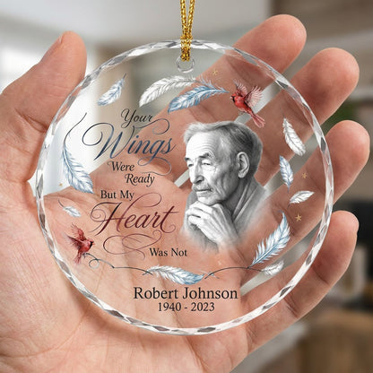 Round glass ornament with sketch portrait, two red cardinals, blue and brown feathers, and memorial name and years.