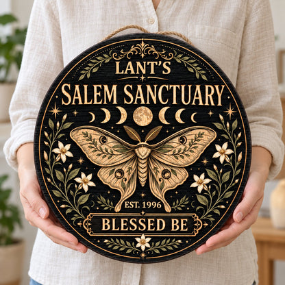 Round wooden sign with a central moth, moon phases, floral vines, stars, and 'Salem Sanctuary' 'Blessed Be' text.