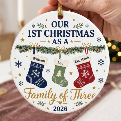 Round white ceramic ornament with garland, three stockings, and 'OUR 1ST CHRISTMAS AS A Family of Three 2026' text with 