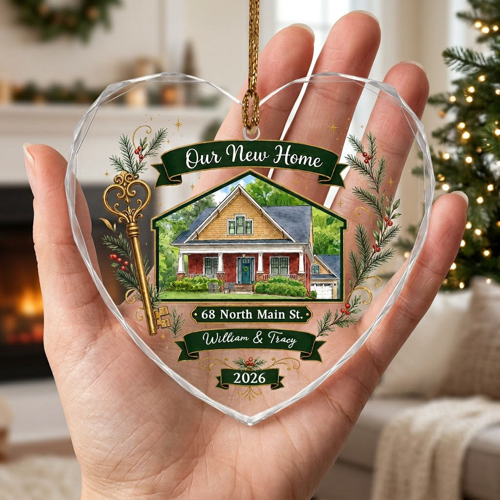 Heart-shaped glass ornament with watercolor house, gold key, evergreens, green banners, and 'Our New Home' text.
