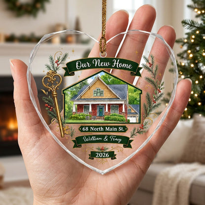 Heart-shaped glass ornament with watercolor house, gold key, evergreens, green banners, and 'Our New Home' text.