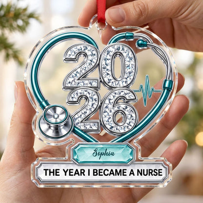 Clear acrylic ornament with a teal stethoscope heart, diamond 2026 numerals, teal ECG wave, and a personalized name bann