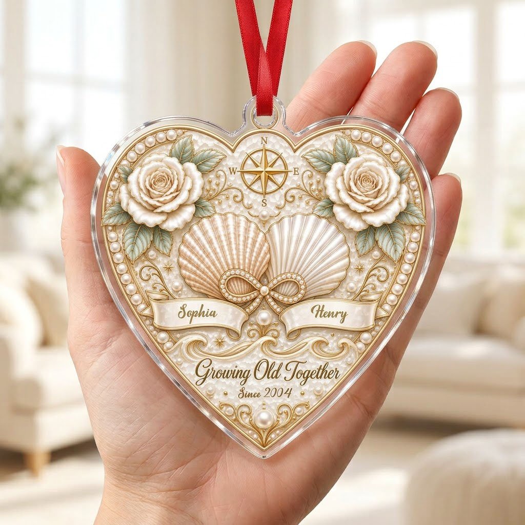 Heart-shaped clear acrylic ornament with seashells, pearl infinity symbol, compass star, and two name ribbons.