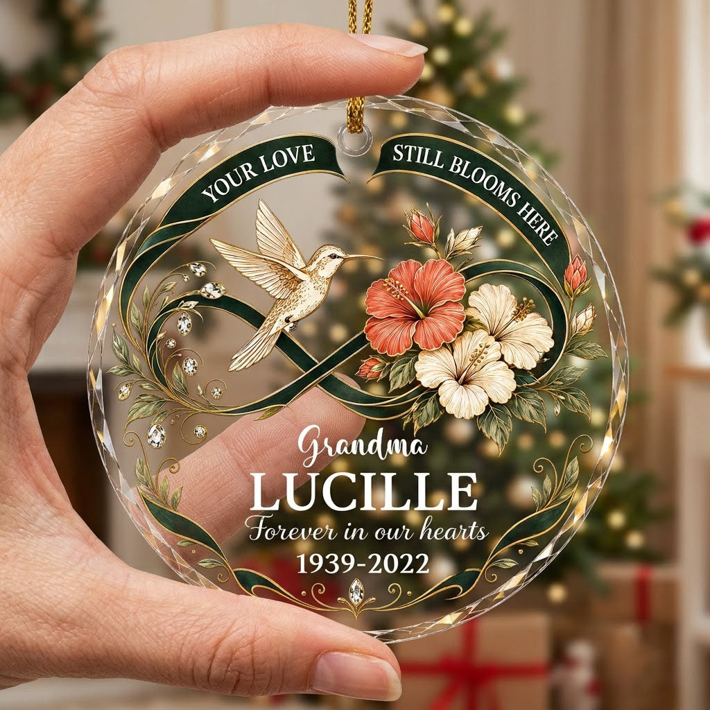 Round glass ornament with hummingbird, hibiscus, green infinity ribbon, and 'Your Love Still Blooms Here' text.