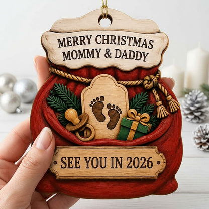Red Santa sack wood ornament with rope tassels, baby footprints plaque, pacifier, and green gift box.