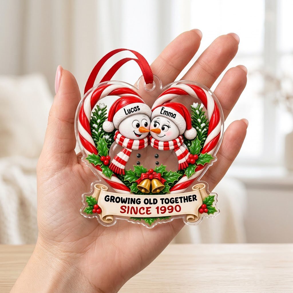Two snowmen touching noses inside a candy-cane heart with holly, gold bells, and a scroll banner with names and year.