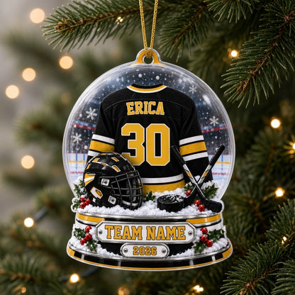Acrylic snow globe ornament with hockey jersey, helmet, crossed sticks, puck, holly, and a silver plaque base.