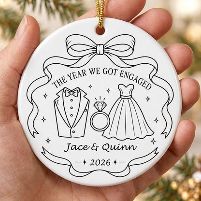 Round white ceramic ornament with black line art of bow, tuxedo, ring, dress, and THE YEAR WE GOT ENGAGED banner.