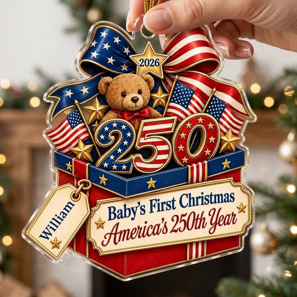 A teddy bear in a red gift box with blue trim, 250 and 2026 with American flags and a patriotic bow on an acrylic orname