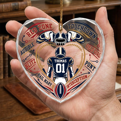 Heart-shaped glass ornament with back-view football player, gold stitched heart frame, football, and play diagram elemen