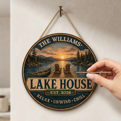 Round wooden sign with lake sunset, two Adirondack chairs on a dock, green canoe, and navy border with wave motifs.