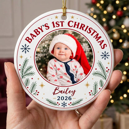 Round ceramic ornament with 'BABY'S 1ST CHRISTMAS', pine sprigs, snowflakes, gold stars, red rings, and a photo frame