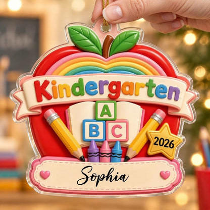 Red apple acrylic ornament with 'Kindergarten 2026', rainbow, ABC blocks, crayons, pencils, star badge, and a name banne