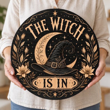 Round wooden sign with 'THE WITCH IS IN' slogan, crescent moon, witch hat, floral borders, stars and scrollwork.