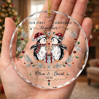 Penguin couple in Santa hats hold gold rings beneath a heart, framed by a pine and gem wreath with a gift box.