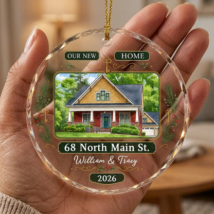 Round glass ornament with watercolor house, green and gold banners, gold key, pine branches, and address and year plaque