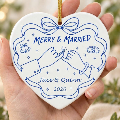 White heart ceramic ornament with blue line art: pinky promise hands, bells, rings, and MERRY & MARRIED text.