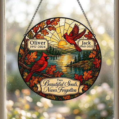 Two red cardinals with a glowing sun over a mountain lake and pine trees, framed by autumn oak leaves on a round suncatc